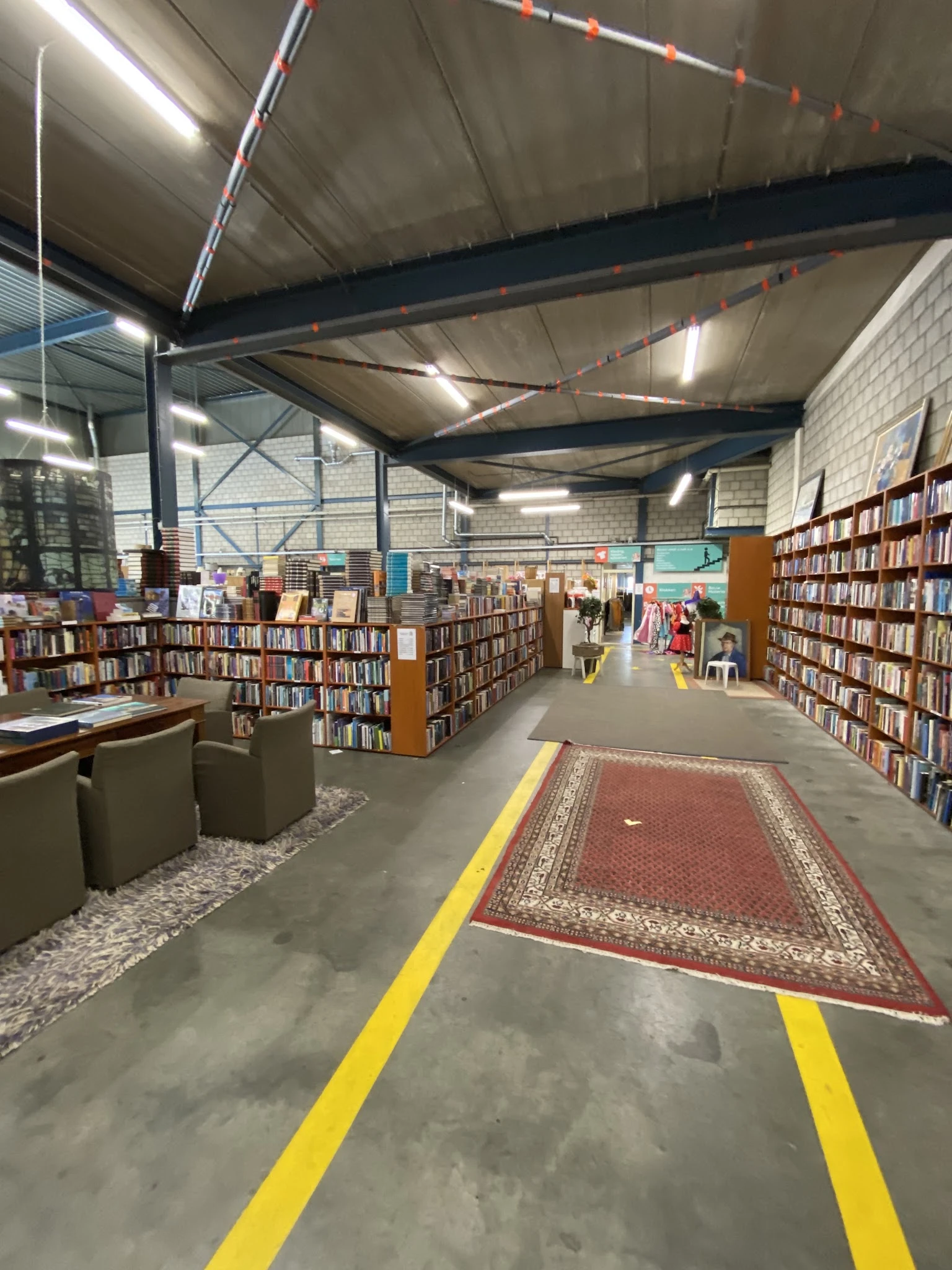 Boekenrekken en boekenkasten langs een gangpad in een grote kringloopwinkelhal met betonnen vloer