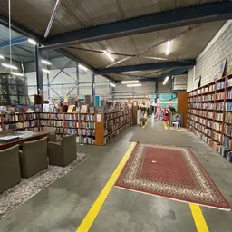 Boekenrekken en boekenkasten langs een gangpad in een grote kringloopwinkelhal met betonnen vloer