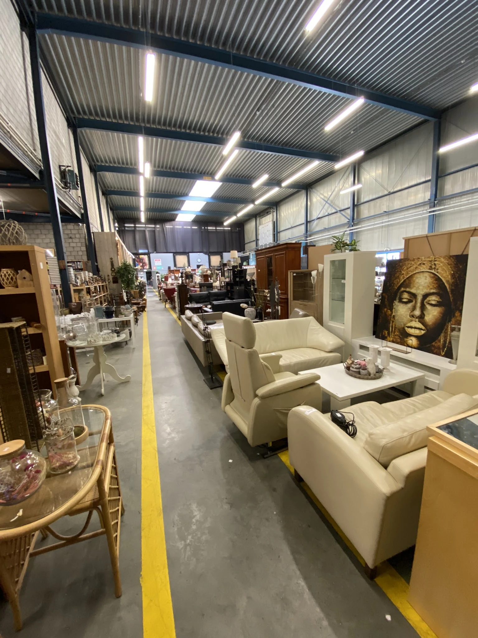 Winkelvloer met uitgestalde meubels waaronder beige stoelen en kasten, goed verlichte ruimte met industrieel plafond