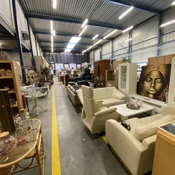 Winkelvloer met uitgestalde meubels waaronder beige stoelen en kasten, goed verlichte ruimte met industrieel plafond