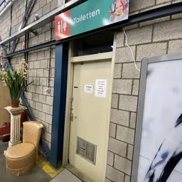 Ingang van kringloopwinkel met gele deur, bloempot en exit-bord zichtbaar