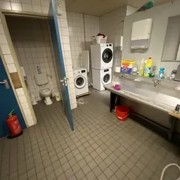 Badkamer met wasmachines, wastafel, toiletruit en schoonmaakspullen op planken