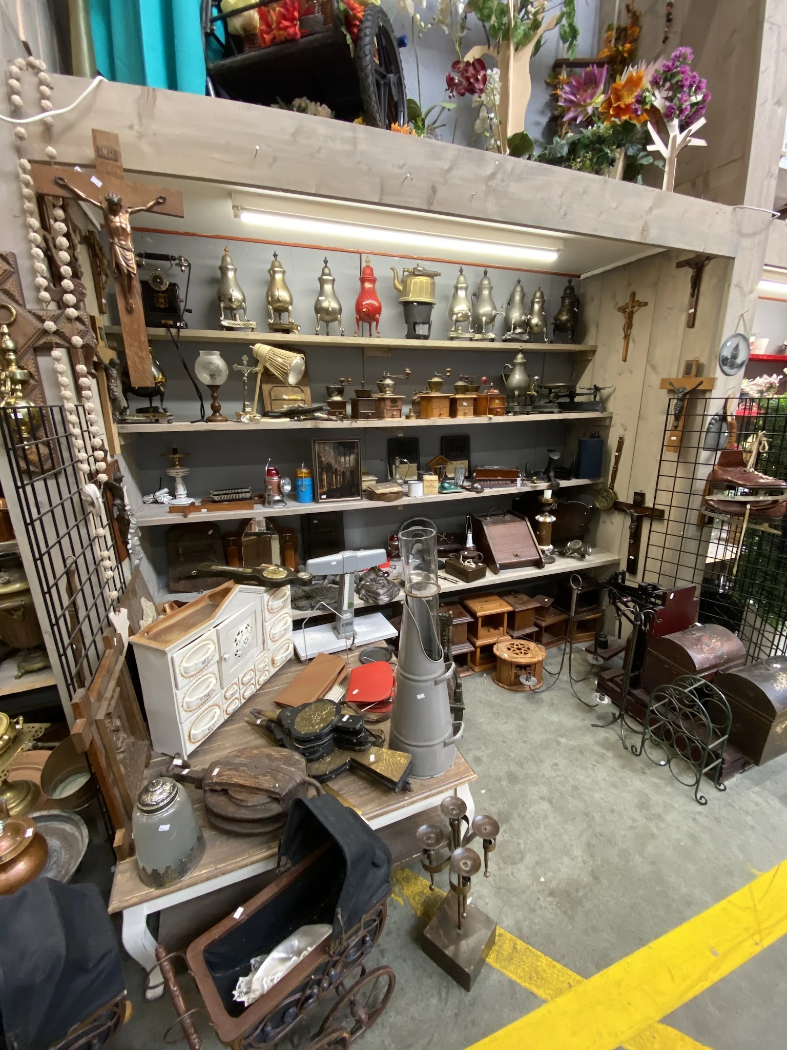 Kringloopwinkel afdeling met stellingen vol huishoudartikelen, decoratie en spullen; op tafel veel rommel en voorwerpen