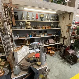 Kringloopwinkel afdeling met stellingen vol huishoudartikelen, decoratie en spullen; op tafel veel rommel en voorwerpen