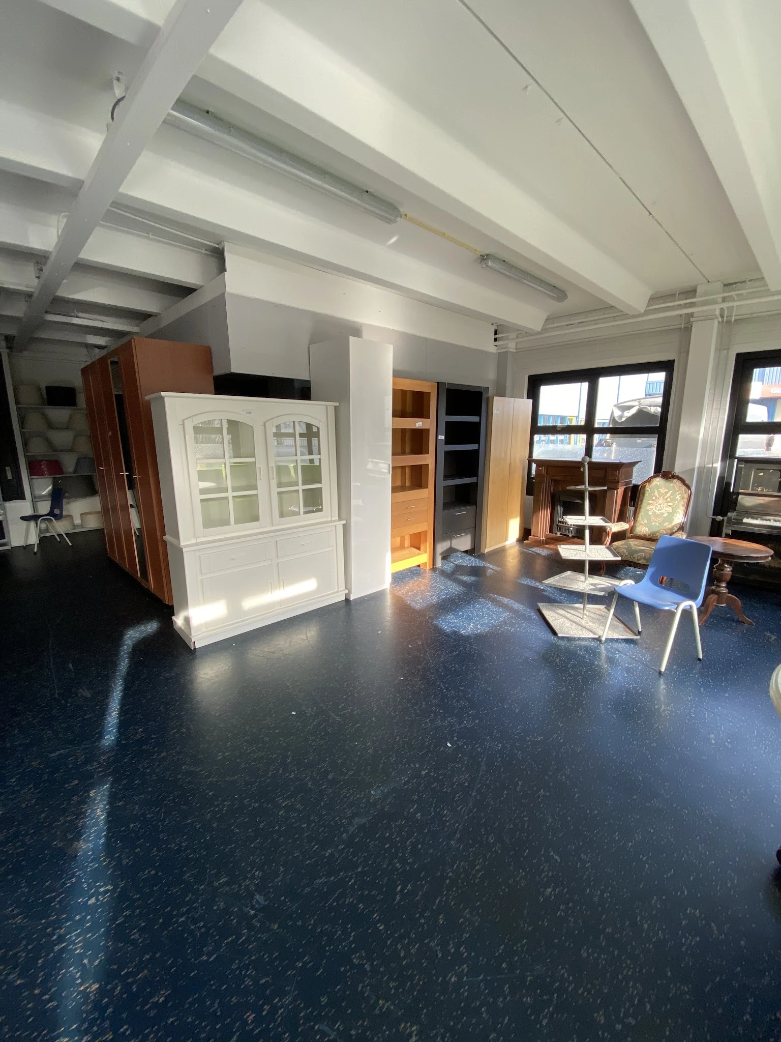 Winkelinterieur met meubelstukken, kasten en stoelen op donkere vloer met ramen op de achtergrond