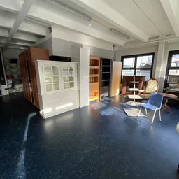 Winkelinterieur met meubelstukken, kasten en stoelen op donkere vloer met ramen op de achtergrond