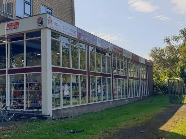 Voorgevel van kringloopwinkel met grote glazen ramen en witte frames, groen grasveld ervoor