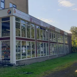 Voorgevel van kringloopwinkel met grote glazen ramen en witte frames, groen grasveld ervoor