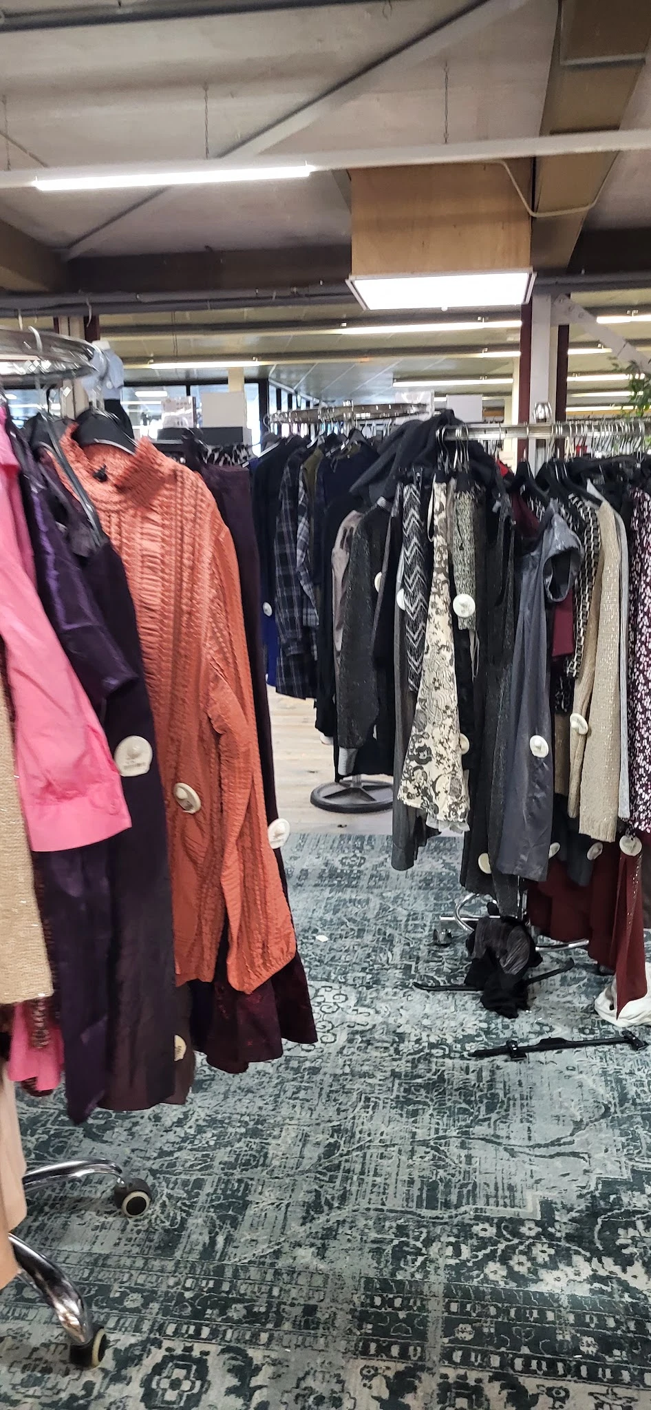 Rekken met tweedehands kleding in verschillende kleuren en stijlen, waaronder jasjes en jurken