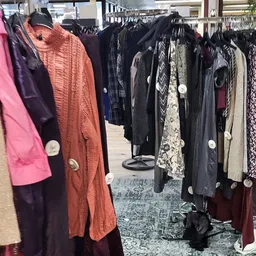 Rekken met tweedehands kleding in verschillende kleuren en stijlen, waaronder jasjes en jurken