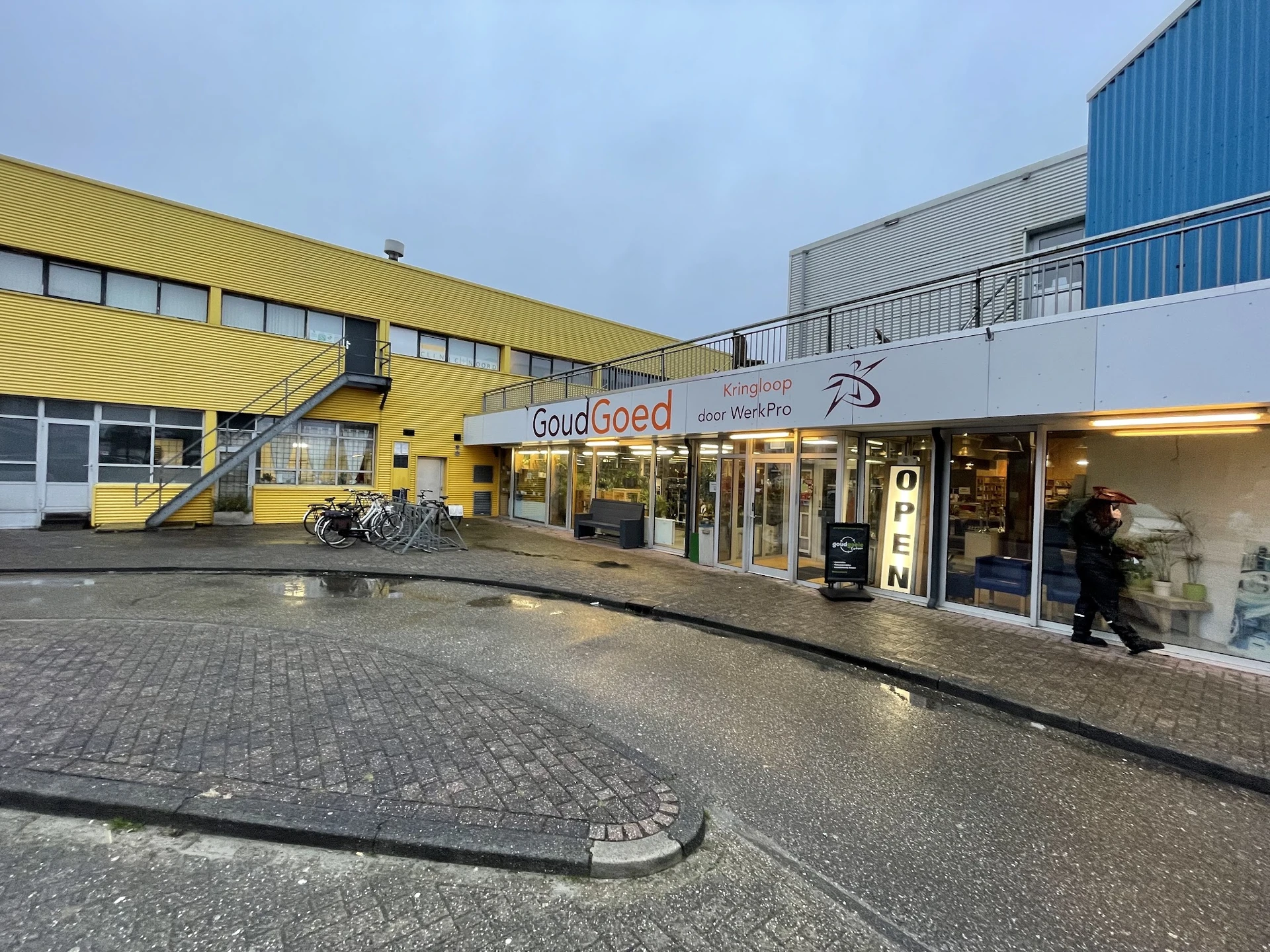 Voorgevel van kringloopwinkel met geel en wit gebouw, ingang met glazen deuren en winkelnaam zichtbaar
