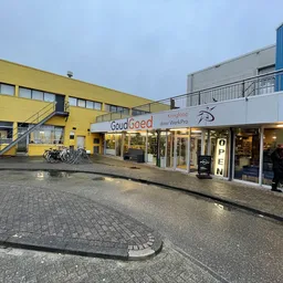 Voorgevel van kringloopwinkel met geel en wit gebouw, ingang met glazen deuren en winkelnaam zichtbaar