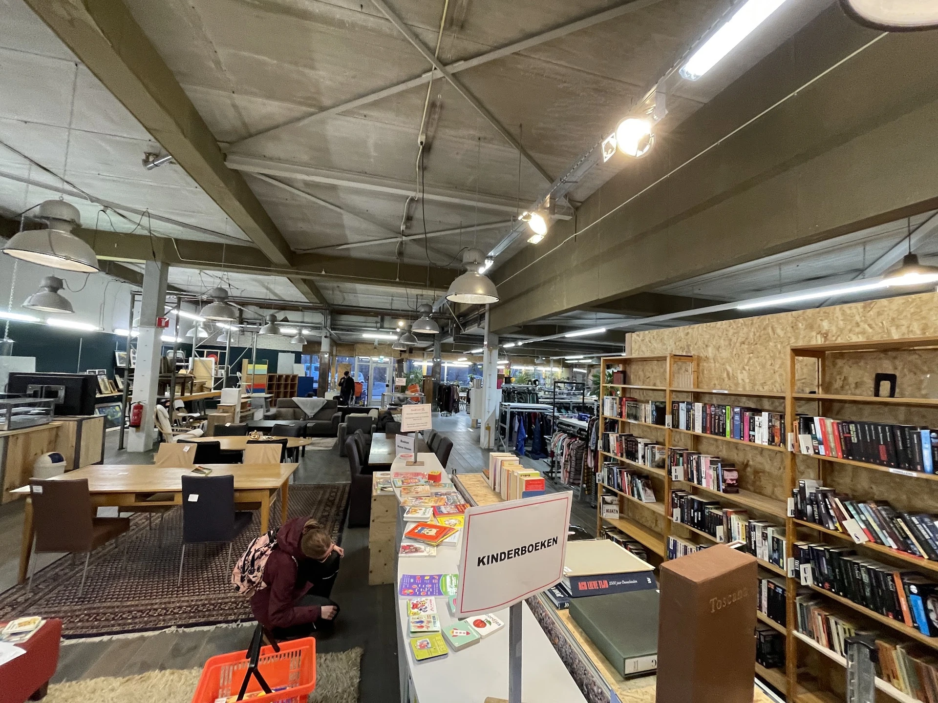 Ruim winkelbinnenland met boekenkasten, tafels met spullen, en hoog plafond met industriële verlichting