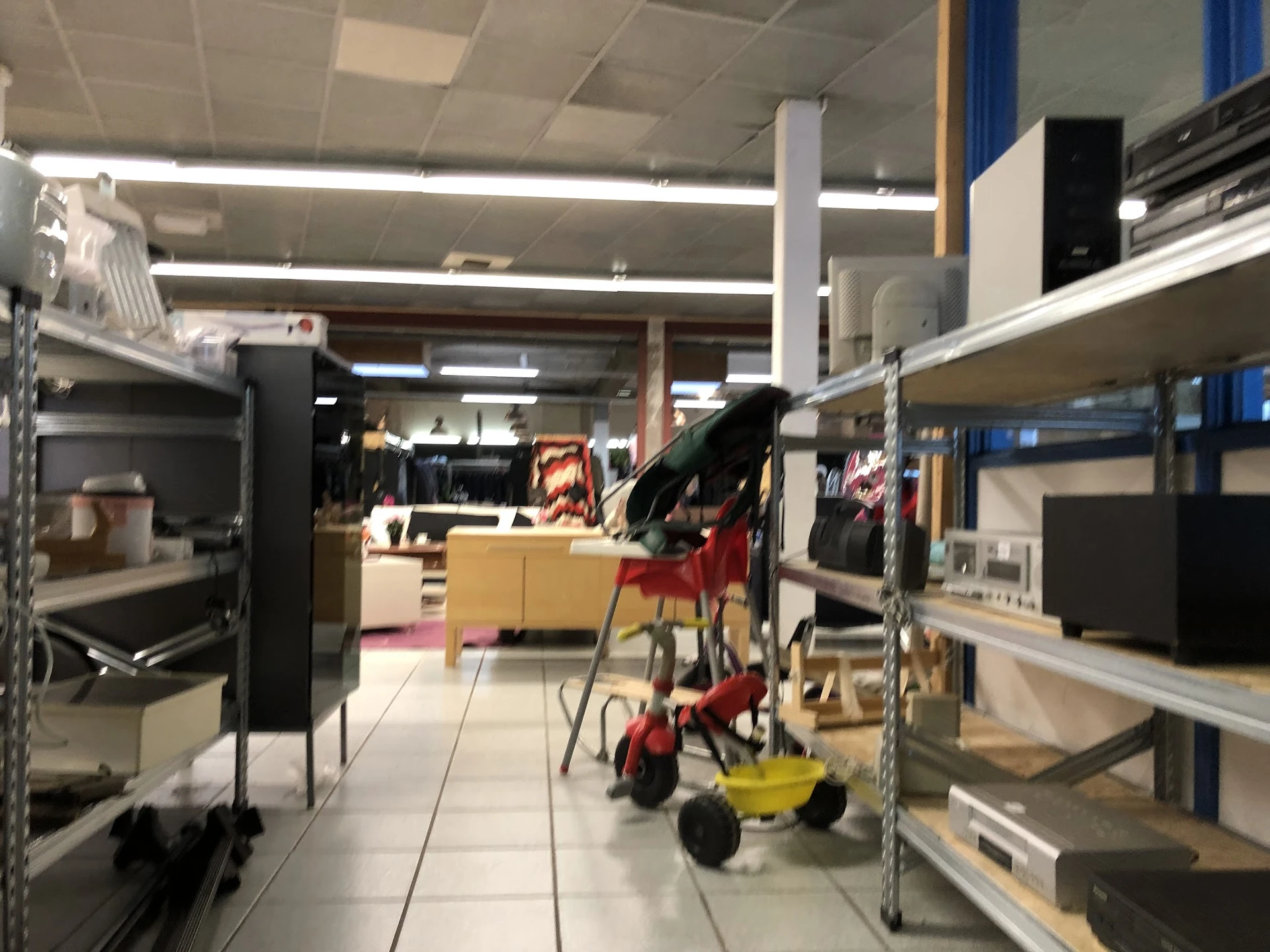 Winkelinterieur met stellingen, rekken met artikelen en een rode winkelwagen op de tegel vloer
