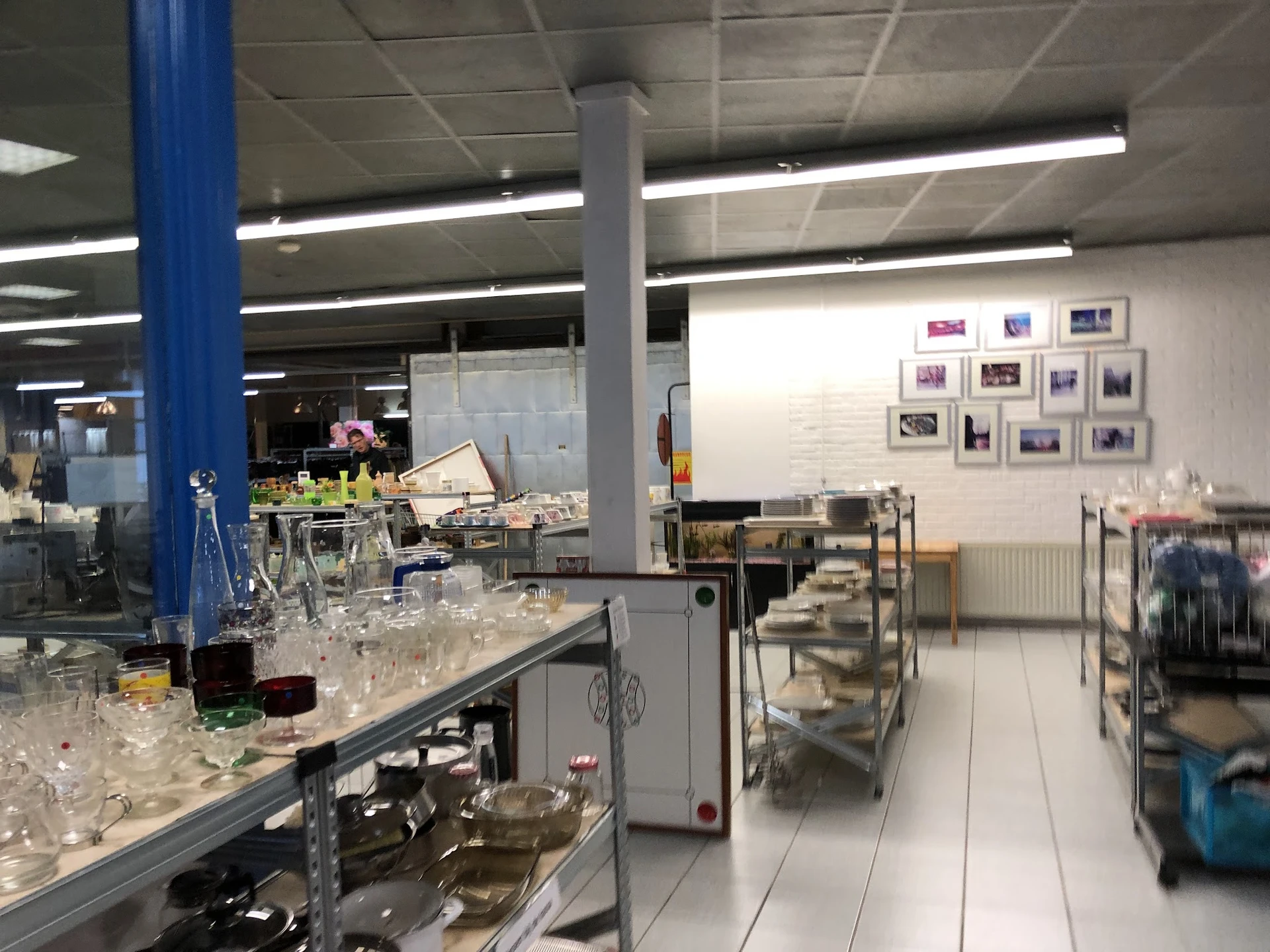 Winkelinterieur met glazen serviesgoed op toonbanken, blauwe pijler, stellingen en wandfoto's