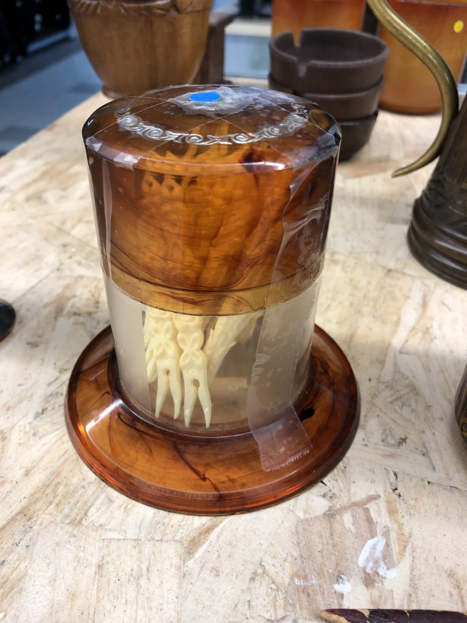 Glazen stolp met houten voet, bevat een wit sculptuur van menselijke figuren