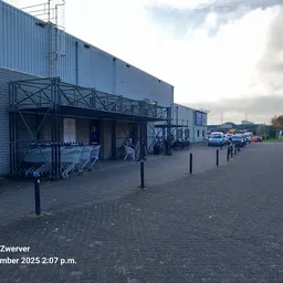 Exterieur van kringloopwinkel met blauwe golfplaten gevel, metalen overkapping en ingang met mensen
