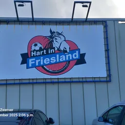 Gevel van kringloopwinkel Hart in Friesland met blauw logo en paardrij-motief op bord