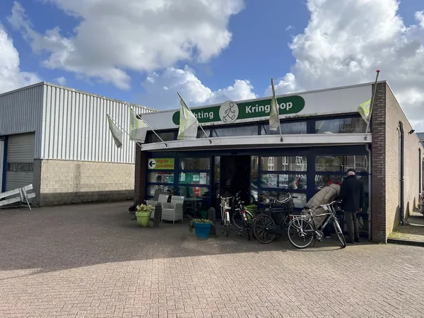Gevel van Kringhop kringloopwinkel met donkere puien en groene letters op het bord, enkele klanten buiten met fietsen