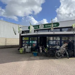 Gevel van Kringhop kringloopwinkel met donkere puien en groene letters op het bord, enkele klanten buiten met fietsen