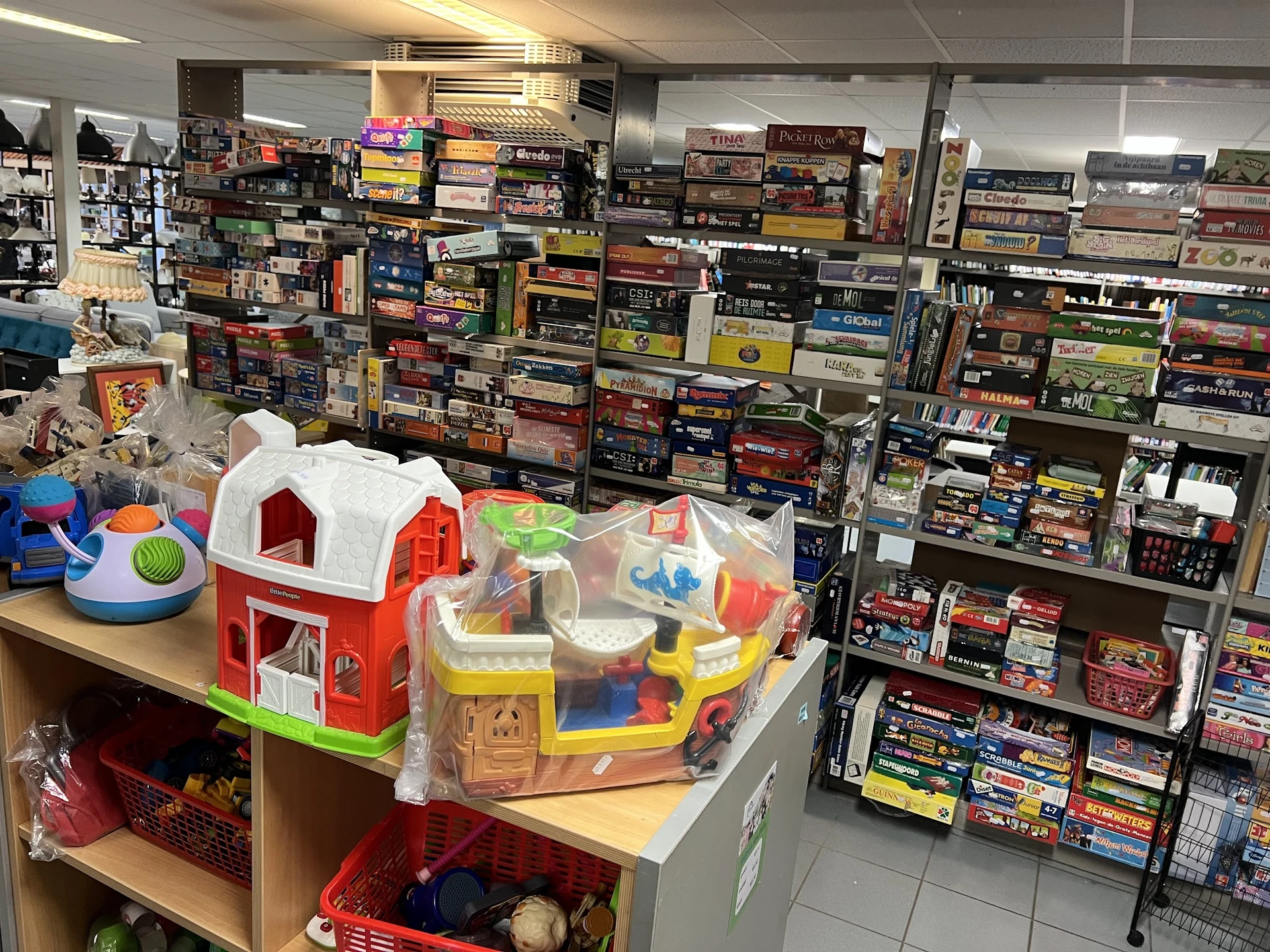 Kinderspeelgoed en bouwblokken op een tafel met kastjes vol dozen met bordspellen en dvd's op de achtergrond
