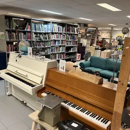 Binnenaanzicht van kringloopwinkel met pianino's, boekenkasten, zithoek en diverse spullen