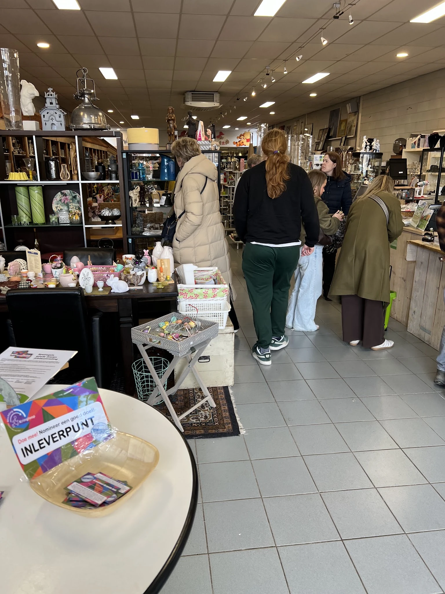 Winkelinterieur met bezoekers tussen stellingen met huishoudelijke artikelen en decoratie