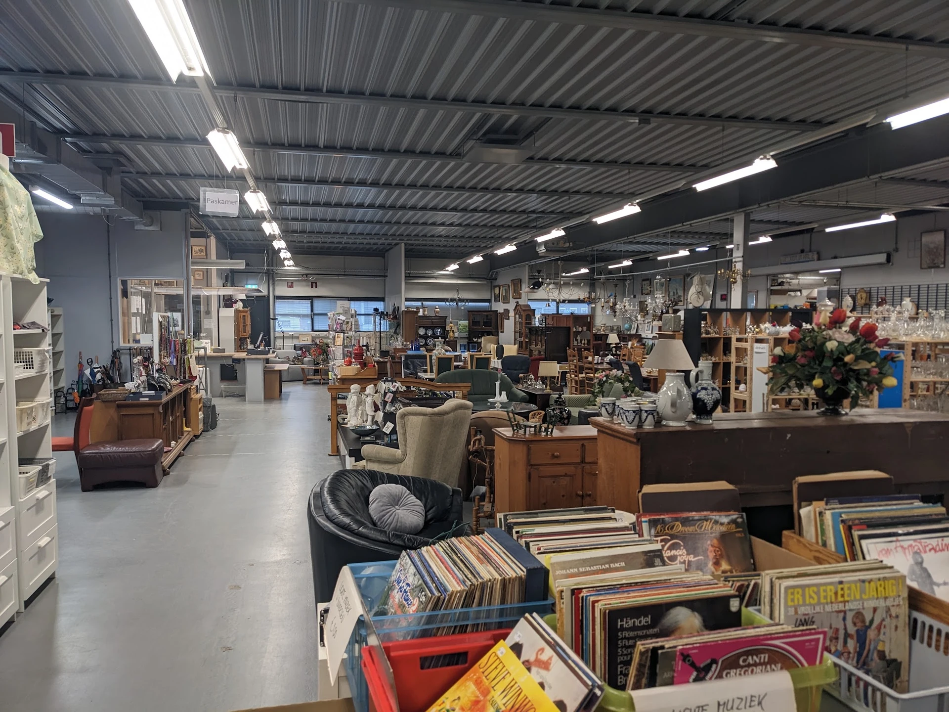 Binnenaanzicht van kringloopwinkel met diverse meubels, boeken, decoratie en spullen op stellingen en in dozen