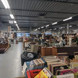 Binnenaanzicht van kringloopwinkel met diverse meubels, boeken, decoratie en spullen op stellingen en in dozen