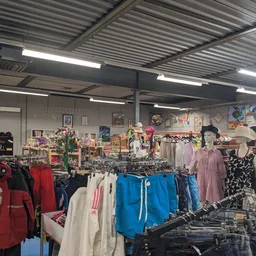 Winkelvloer met rekken vol tweedehands kleding, verlicht met TL-buizen, achtergrond met decoratie en verdere artikelen
