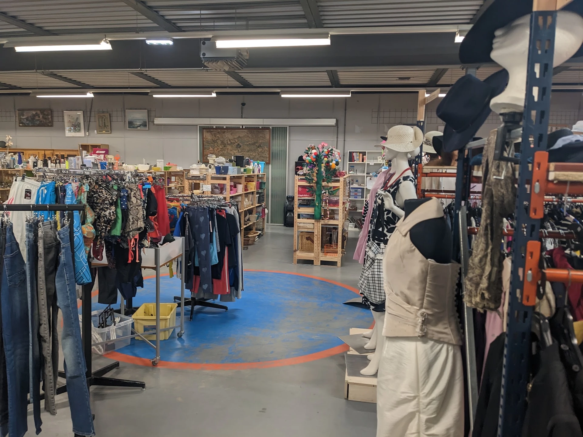 Winkelvloer van kringloopwinkel met kledingrekken, mannequins en winkelrekken met diverse artikelen