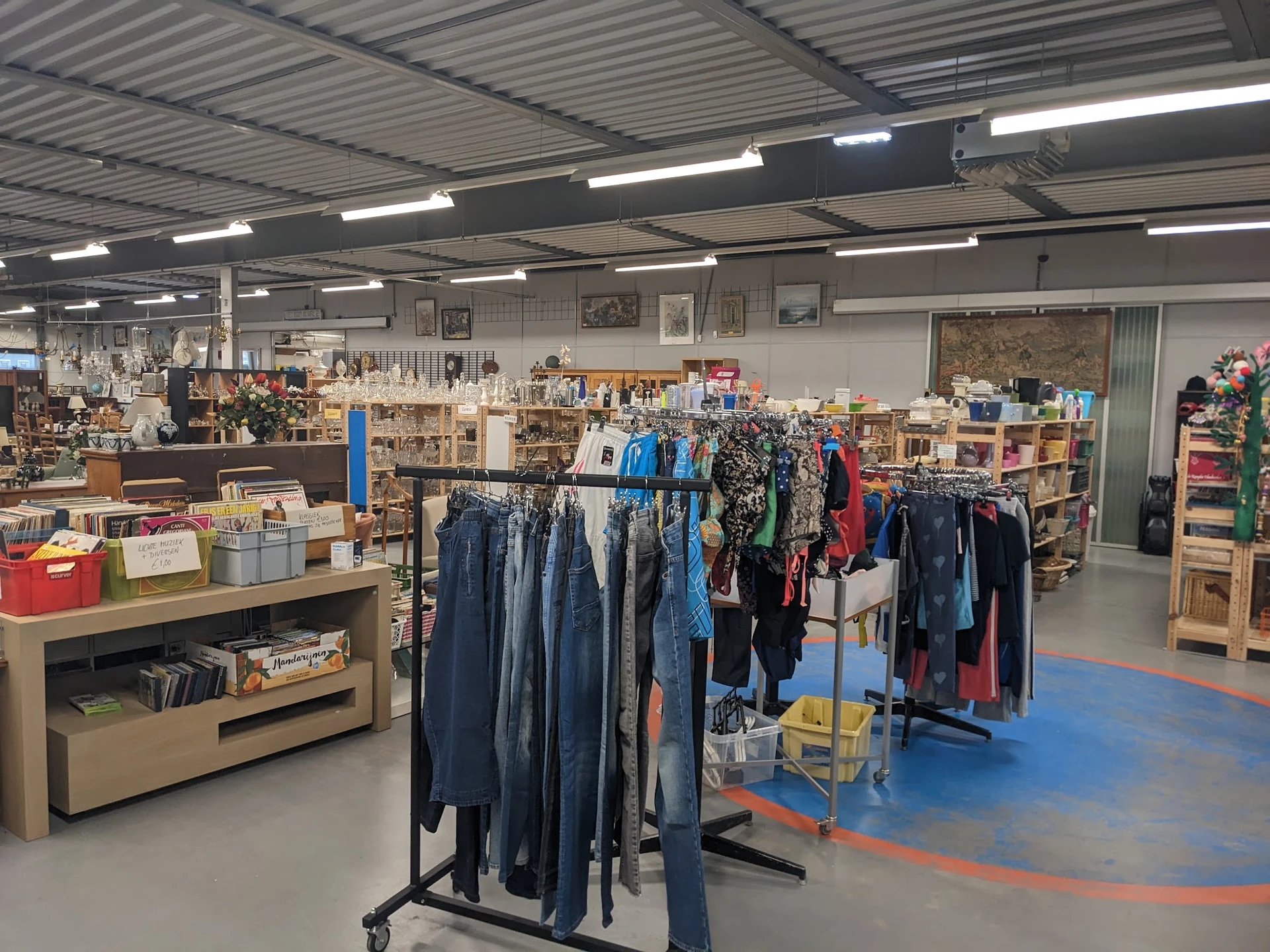 Winkelvloer met kledingrekken, stellingen met artikelen en blauwe vloermarkeringen in een kringloopwinkel
