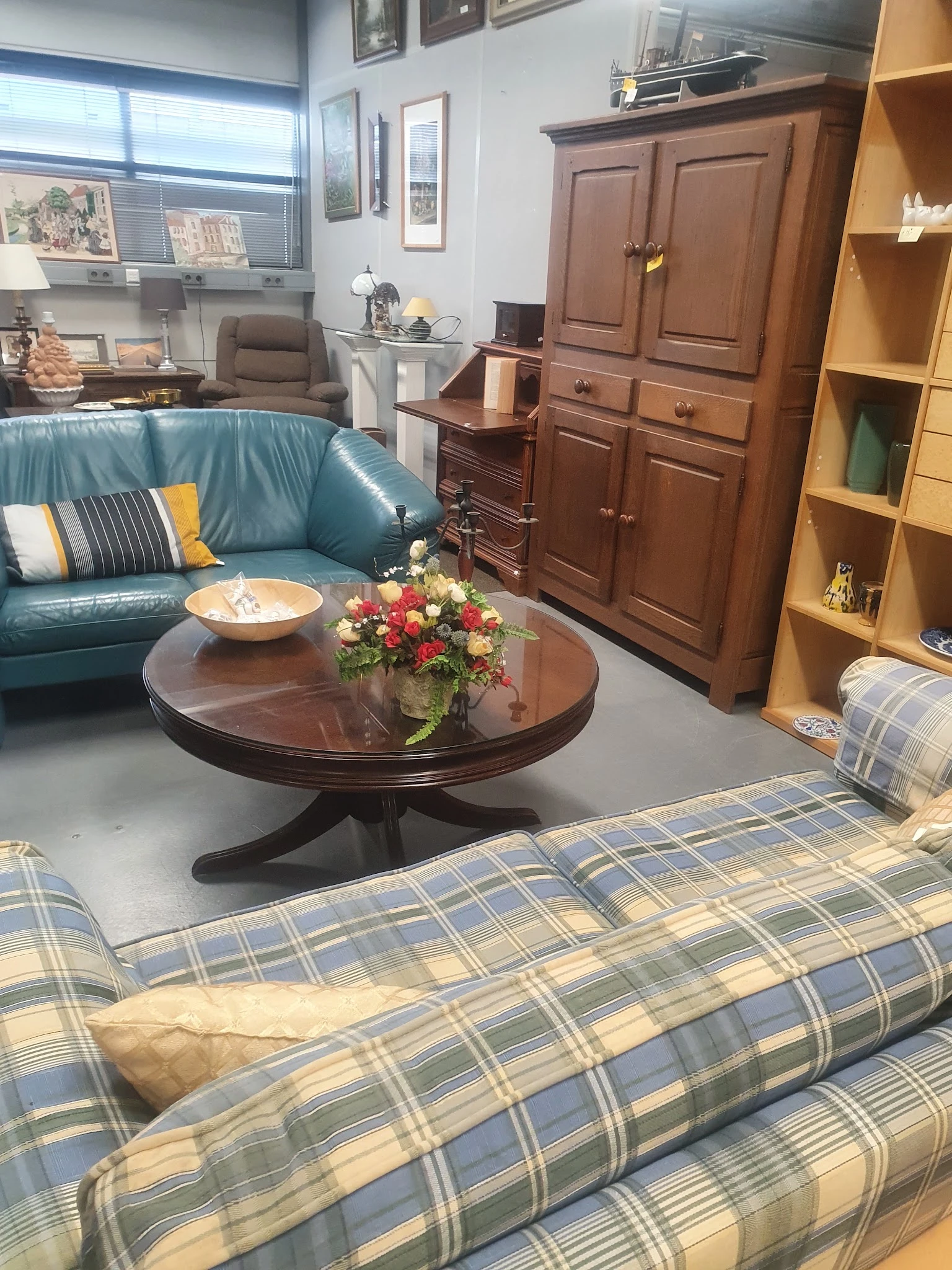 Sfeervolle woonkamer inrichting met blauw leren bankje, ronde houten salontafel met bloemen, gele boekenkast en houten kast