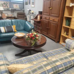 Sfeervolle woonkamer inrichting met blauw leren bankje, ronde houten salontafel met bloemen, gele boekenkast en houten kast