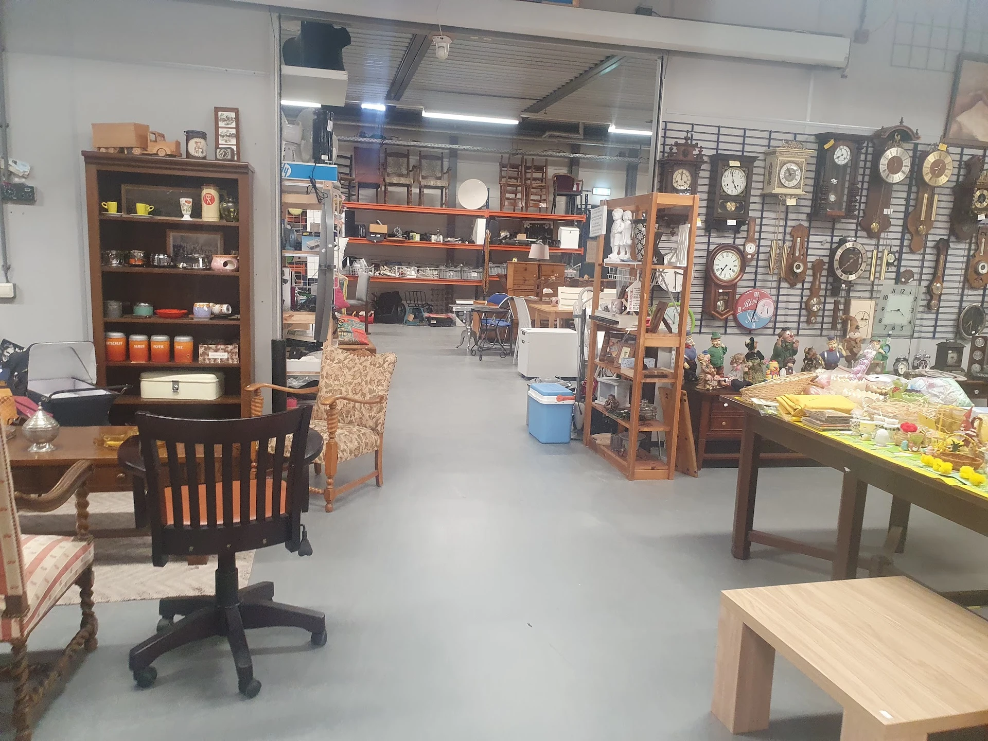 Overzicht van de winkelvloer met houten meubels, stellingen, een zwarte bureaustoel, diverse artikelen en decorstukken