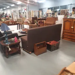 Meubels in de winkel: bruine fauteuil, houten tafels, houten kasten en opbergmanden.
