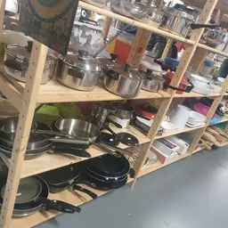 Houten stellingkast met diverse kookgerei: pannen, potten, wokpannen en andere keukengerei netjes uitgestald.