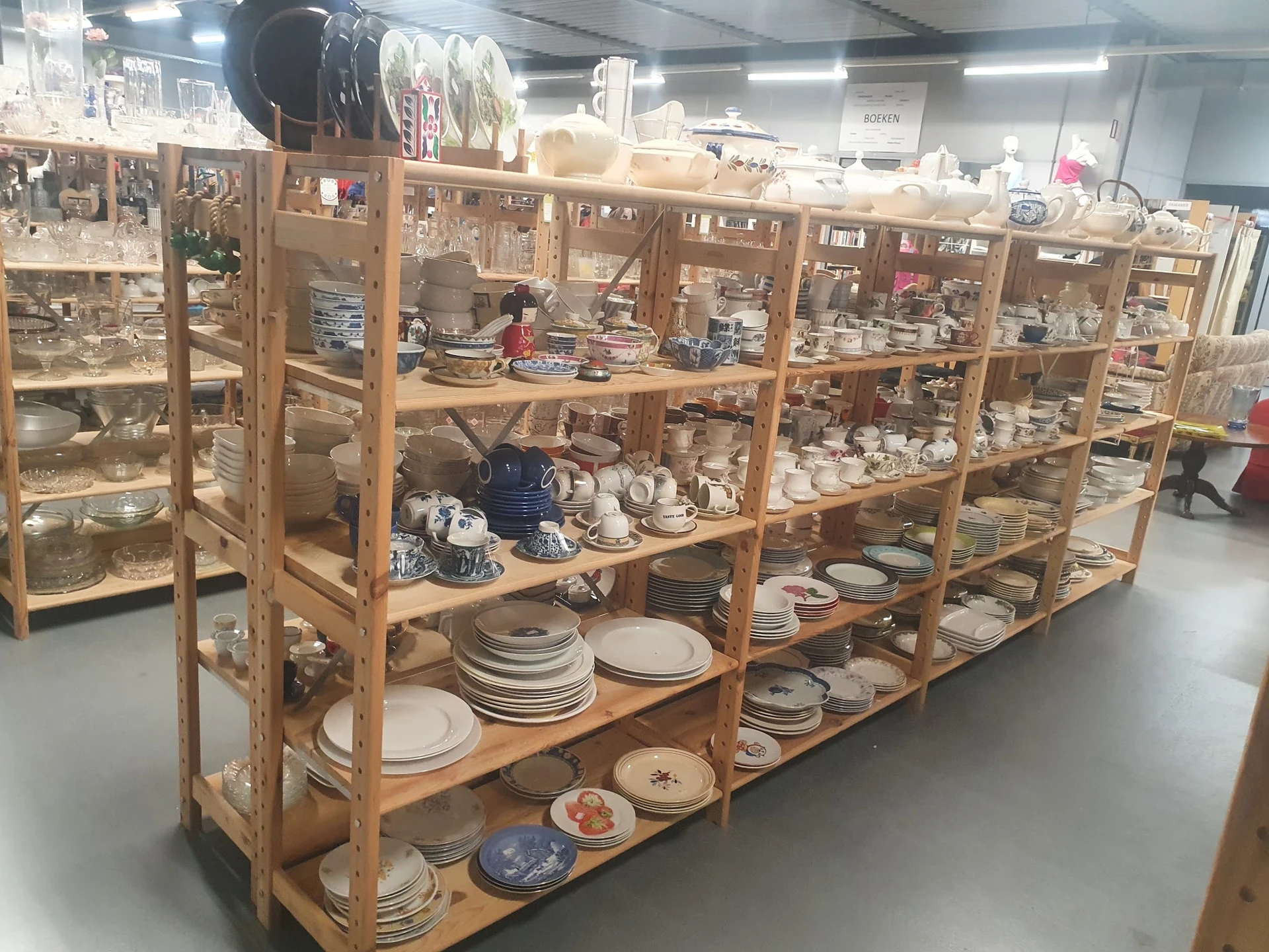 Houten vitrinekast met diverse serviesgoed, borden, kopjes en decoratieve items uitgestald op meerdere planken