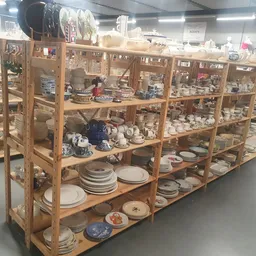 Houten vitrinekast met diverse serviesgoed, borden, kopjes en decoratieve items uitgestald op meerdere planken