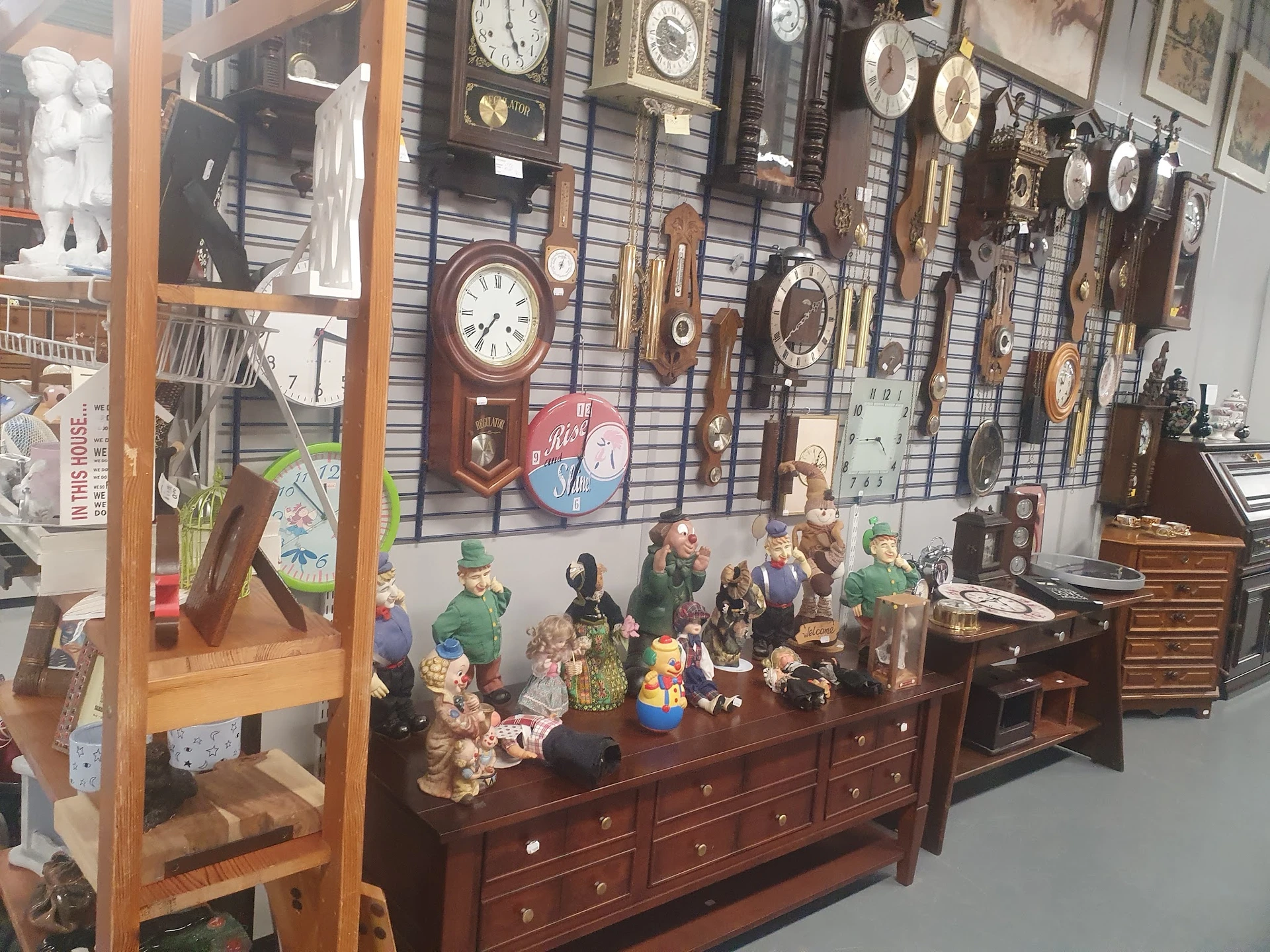 Antieke klokken, beeldjes en huishoudelijke artikelen op een houten dressoir en aan de muur
