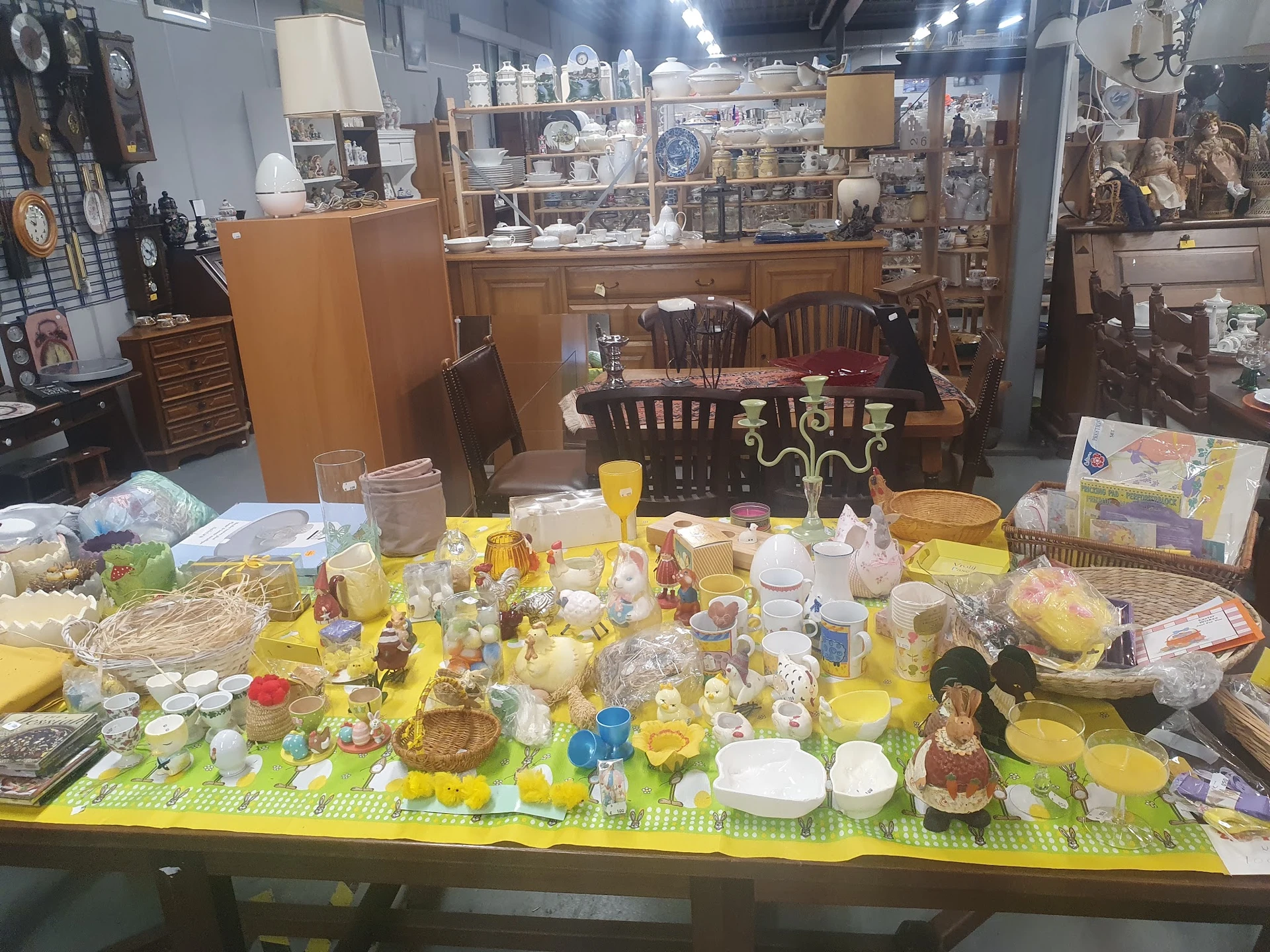 Uitgestalde gele huishoudelijke artikelen, servies en keukenbenodigdheden op een tafel in de kringloopwinkel