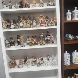 Drie planken met verzameling keramische beeldjes en decoratieve porseleinen objecten