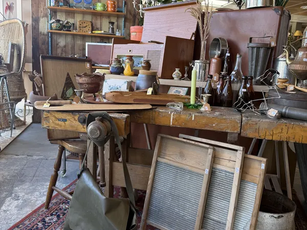 Winkelbinnenruimte met houten werkbank, vintage items, meubels en diverse tweedehandsartikelen op stellingen