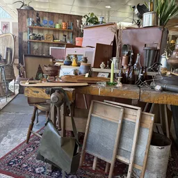 Winkelbinnenruimte met houten werkbank, vintage items, meubels en diverse tweedehandsartikelen op stellingen