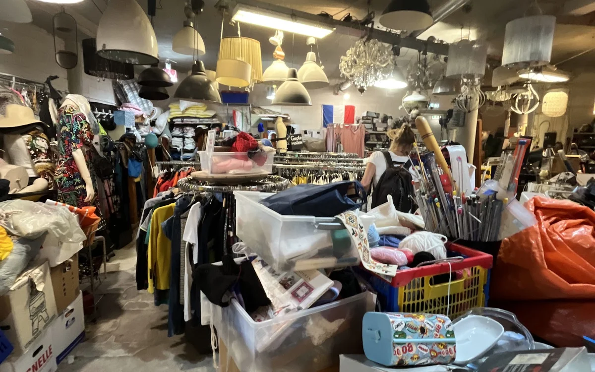 Winkelvloer met rekken kleding, tafels vol spullen, lampen en huishoudartikelen in een kringloopwinkel