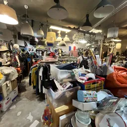 Winkelvloer met rekken kleding, tafels vol spullen, lampen en huishoudartikelen in een kringloopwinkel