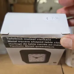 Verpakt metalen vierkant tafelklokje in doosje, met prijssticker €7.50