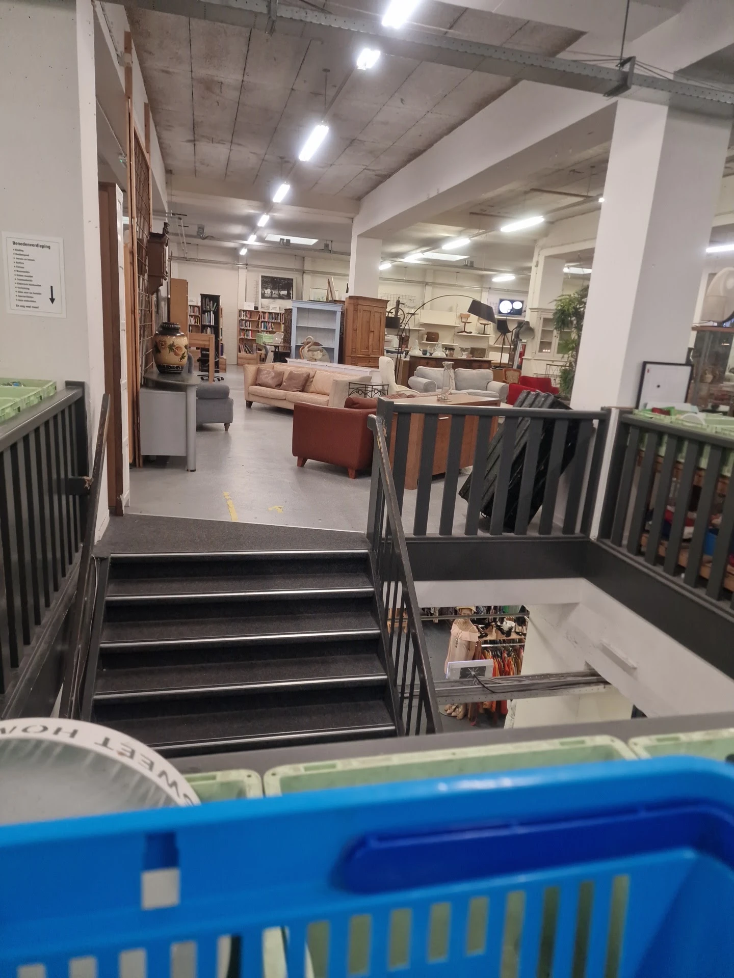 Trappenhuisaanzicht in kringloopwinkel met zicht op winkelvloer met meubels en inrichting
