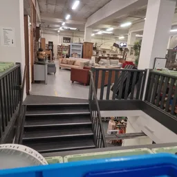 Trappenhuisaanzicht in kringloopwinkel met zicht op winkelvloer met meubels en inrichting