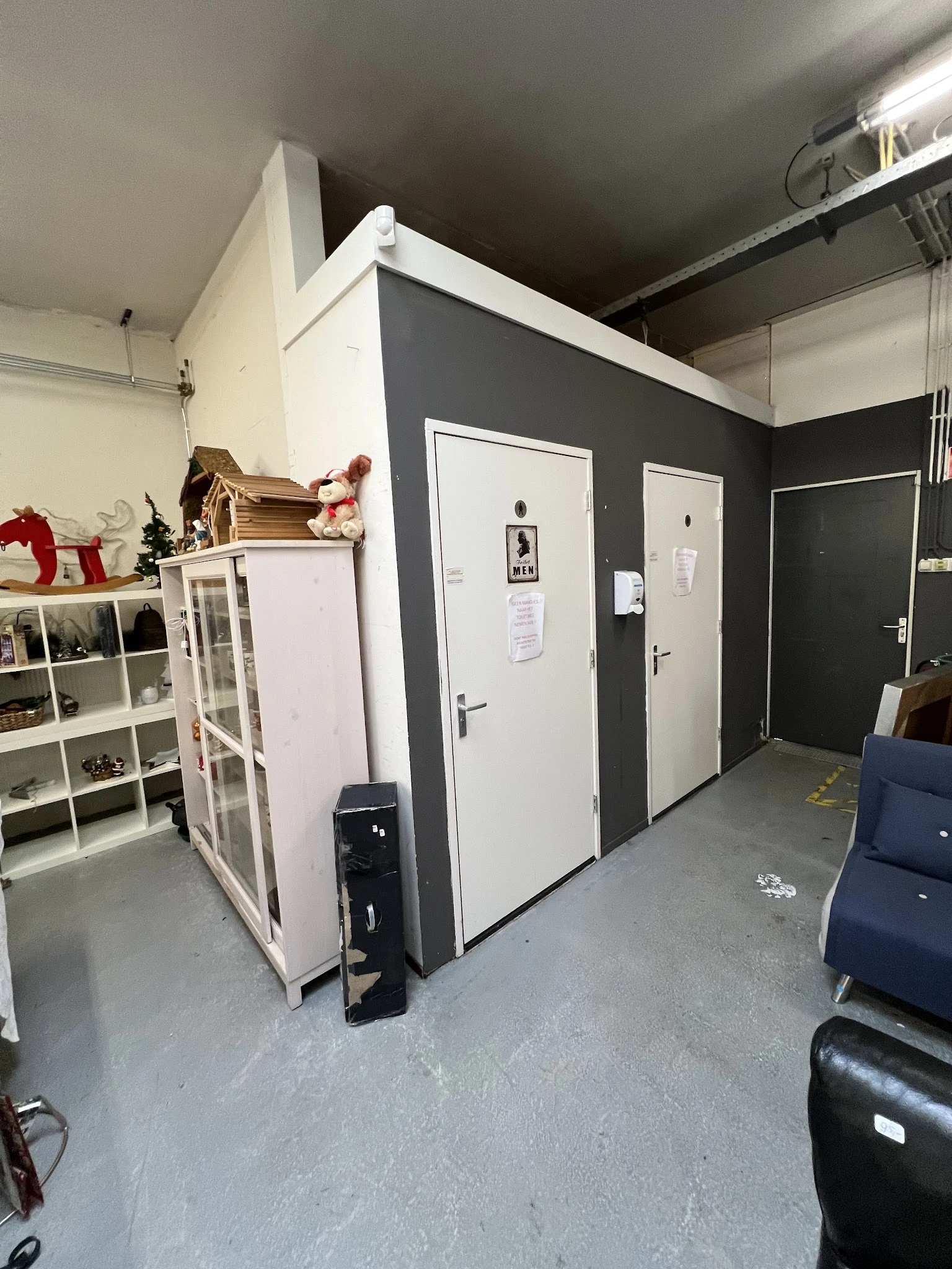 Binnenzicht van kringloopwinkel met witte kastjes, donkergrijze wanden en witte deuren